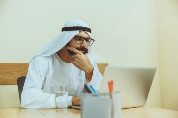 Arab saudi businessman working online with a laptop and tablet in his comfortable cabinet or office. Male model as an enterpreneur. Concept of business, finance, modern technologies, start up, economy.